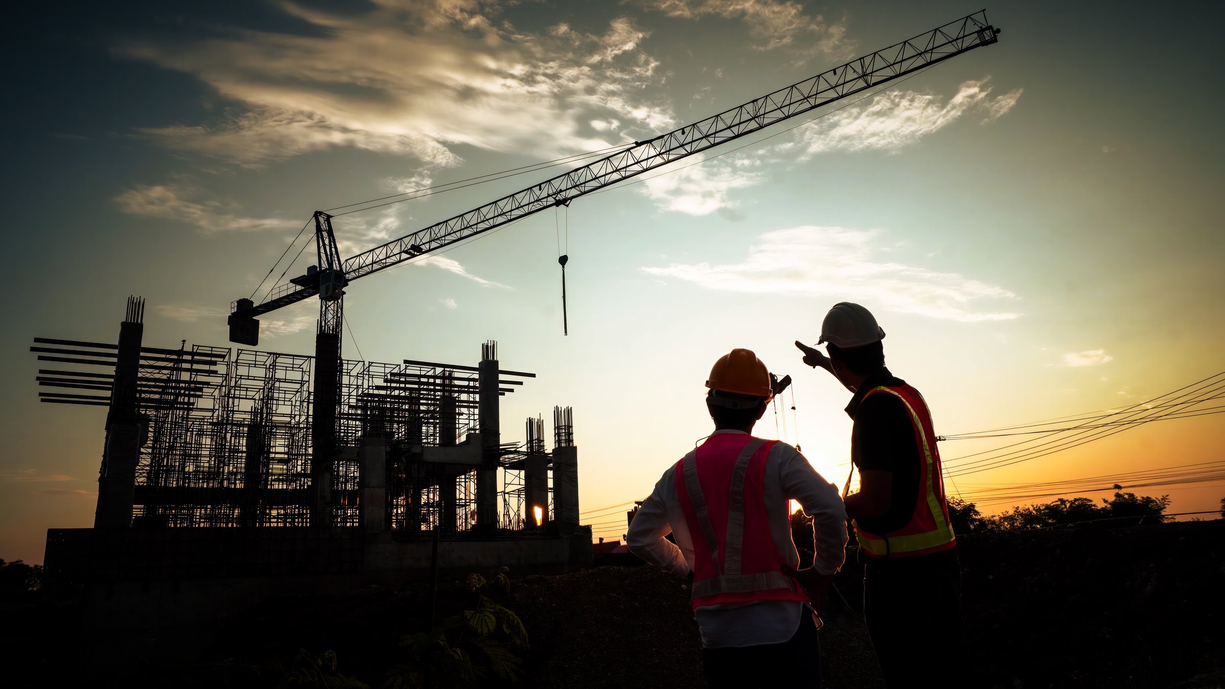 Silhouette of team engineer using laptop to control work, crane, construction site.